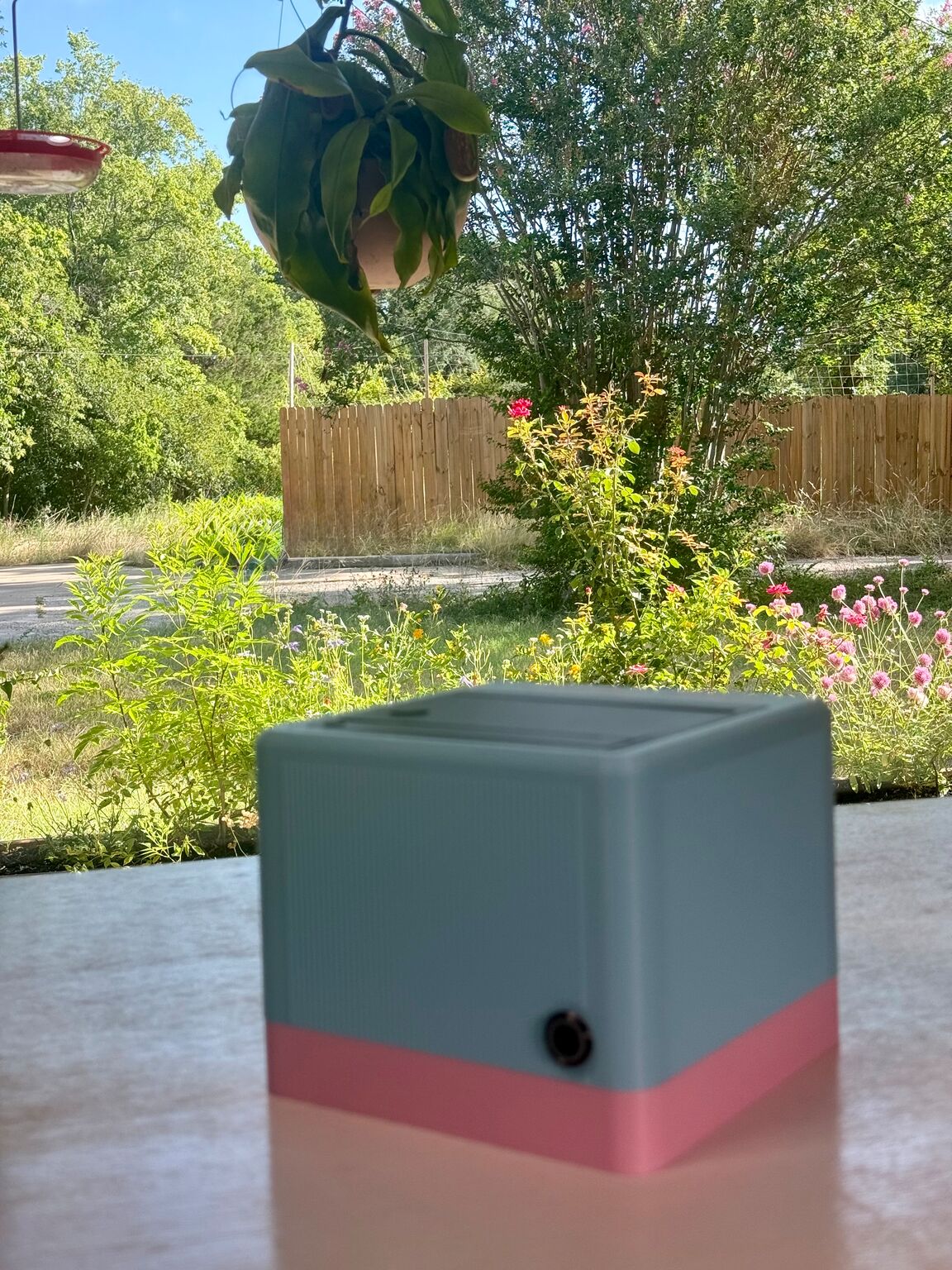 A teal-and-pink StickyFax on a patio table in front of a sunny wildflower garden